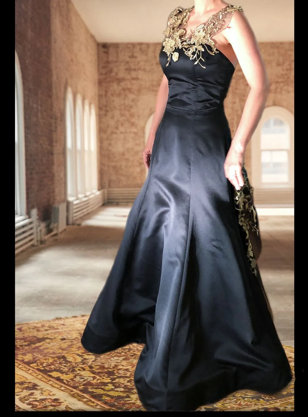 Full-length black satin gown with gold embroidered floral detail across one shoulder.