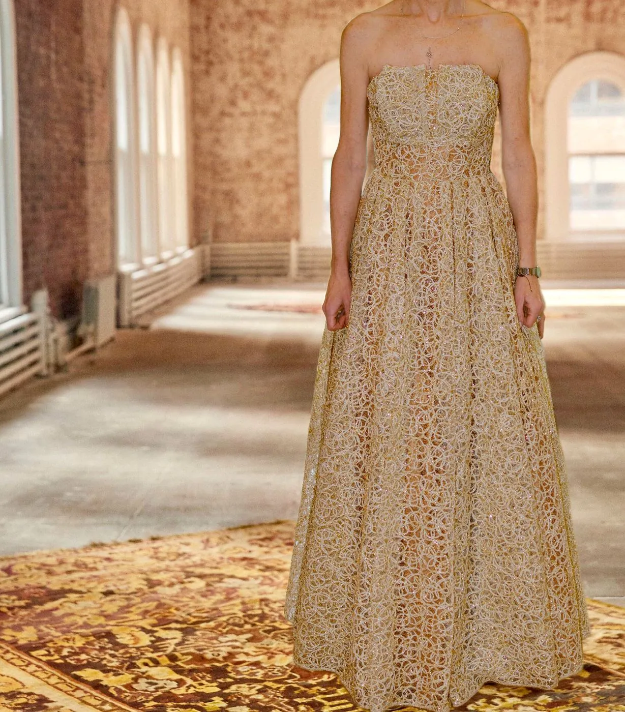 Gold guipure lace ball gown with a full skirt, photographed in a sunlit hall.