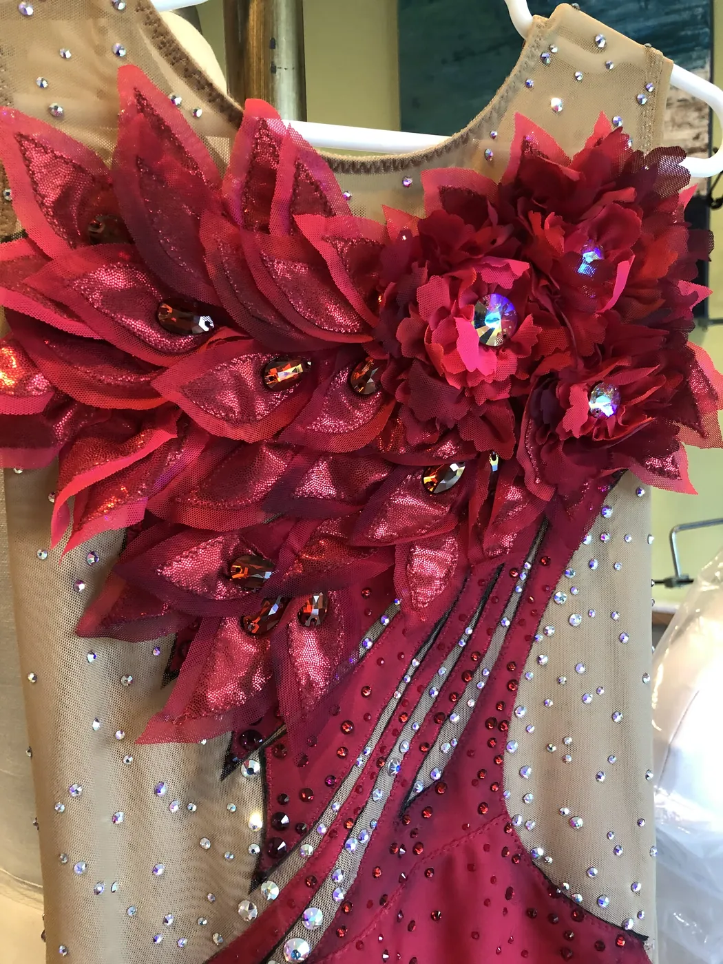 Close detail of hand-cut fabric petals and set crystals on a competition leotard.