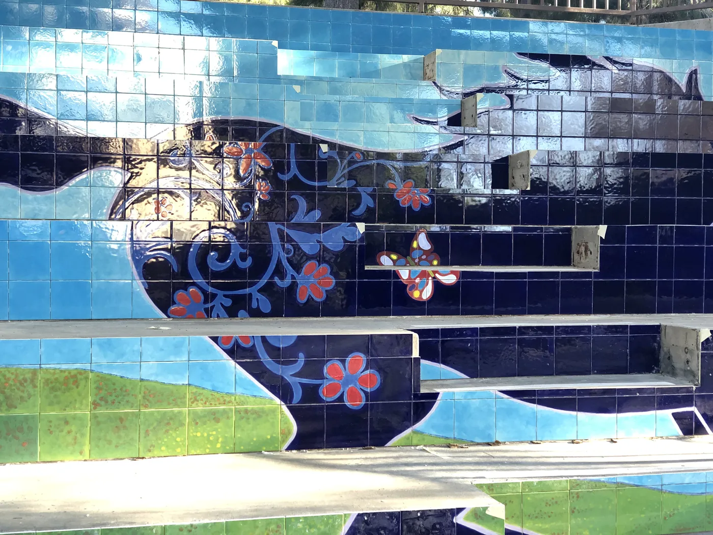 Tiled mural of a galloping navy horse with painted flowers, set into a pool wall.